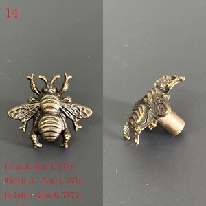 Puede incluir: Pomo de armario con forma de abeja de color bronce. El pomo mide 4 cm de largo, 3,5 cm de ancho y 2 cm de alto. La abeja presenta alas y segmentos corporales detallados. La imagen muestra el pomo desde dos &aacute;ngulos.