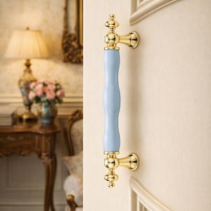 May include: A gold-toned door pull with a light blue center section. The pull is mounted on a cream-colored door. The design is ornate and classic, with a decorative style. The door pull is a decorative hardware element.