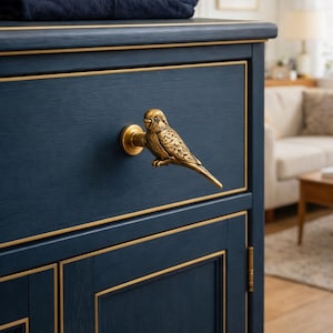Puede incluir: Un mueble azul marino con detalles dorados y un tirador en forma de pájaro. El tirador es una escultura detallada en metal dorado. El mueble tiene una pila de camisas dobladas encima. Medidas en centímetros.