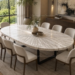 May include: An oval dining table with a white and gray inlaid stone surface featuring a sunburst pattern, supported by a black metal frame. The table is surrounded by eight chairs with off-white upholstered seats and dark wooden frames.