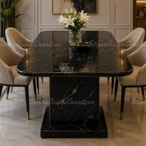 Puede incluir: Una mesa de comedor rectangular con una superficie de mármol negro pulido con vetas blancas y una base de pedestal a juego. La mesa está rodeada por cuatro sillas tapizadas en beige con costuras verticales y patas negras con detalles dorados.