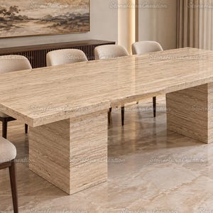 Puede incluir: Una mesa de comedor rectangular hecha de piedra travertino beige pulida, con una superficie lisa y brillante con vetas lineales naturales y dos bases de pedestal robustas en forma de bloque que sostienen el tablero.