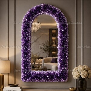 Pode incluir: Um espelho de parede arqueado com uma moldura espessa e texturizada composta por numerosos cristais de ametista roxo-escuro. O espelho reflete o interior de uma sala com um lustre, um sofá curvo e uma planta. A moldura tem uma borda superior arredondada.
