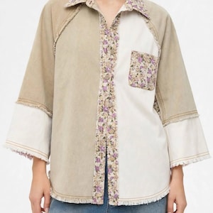 Op de afbeelding: Een overhemd met knoopsluiting in een color-block ontwerp met beige en witte panelen. Het kledingstuk heeft een kraag, knoopsluiting en borstzak met bloemenprint. Driekwartmouwen met witte boorden en gerafelde randen.