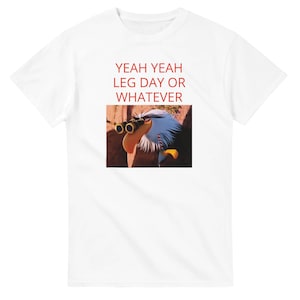 Könnte beinhalten: Weißes T-Shirt mit dem roten Text "YEAH YEAH LEG DAY OR WHATEVER". Das Shirt zeigt ein Cartoon-Bild eines Vogels mit Fernglas. Der Vogel blickt mit einem humorvollen Ausdruck nach oben.