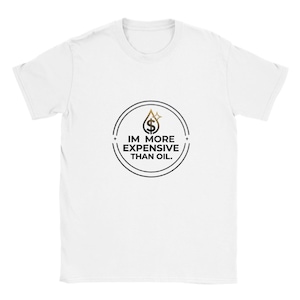 Könnte beinhalten: Weißes T-Shirt mit einem kreisförmigen Aufdruck. Das Design zeigt ein goldenes Dollarzeichen in Tropfenform und den Text "IM MORE EXPENSIVE THAN OIL." Das Design ist in einem schwarzen Kreis eingeschlossen.