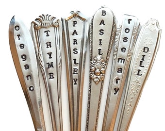 May include: Set of seven silver-toned metal spoons with black lettering, each spoon is labeled with a different herb name: oregano, thyme, parsley, basil, rosemary, and dill.