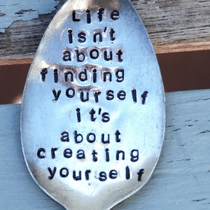 May include: A silver spoon with the words "Life isn't about finding yourself it's about creating yourself" engraved on it.
