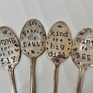 May include: Four silver spoons with engraved sayings about herbs. The spoons read "Thyme for me to fly", "It's Parsley my fault", "Kind of a big dill", and "Mint to be".
