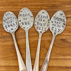 May include: Four silver spoons with decorative handles. Each spoon has a different saying stamped on the bowl: "It's Parsley my Fault", "Mint to Bee", "Kind of a Big Dill", and "Thyme for Me to Fly".