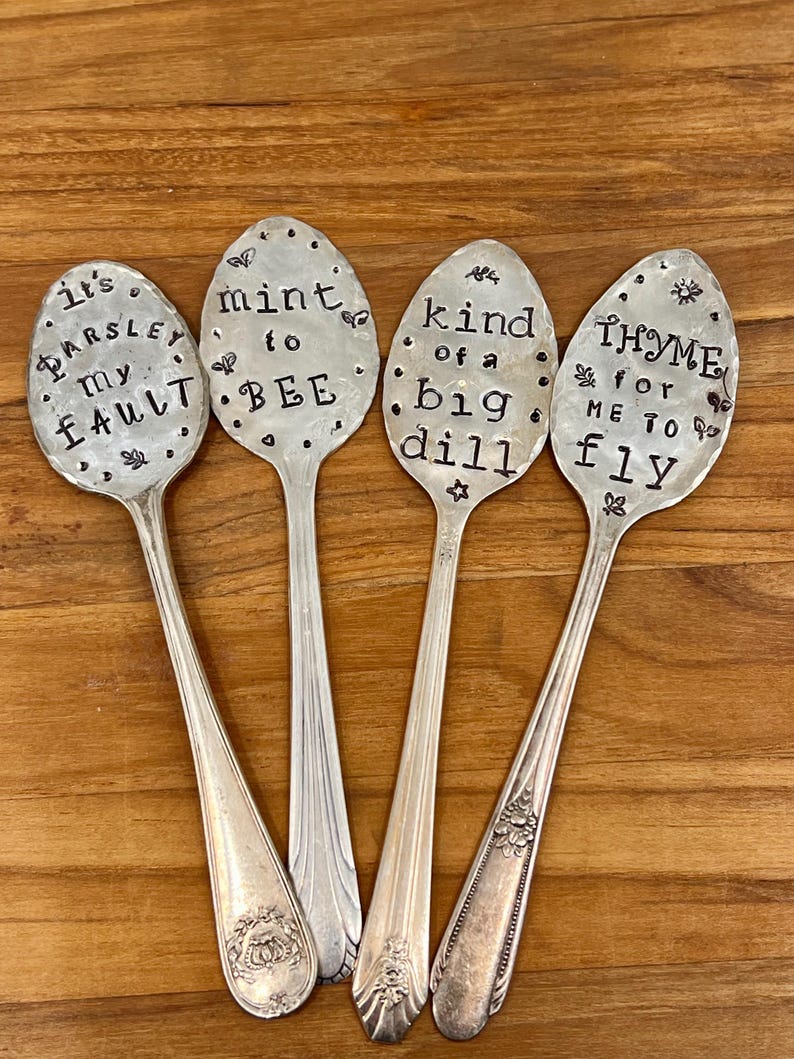 May include: Four silver spoons with decorative handles. Each spoon has a different saying stamped on the bowl: "It's Parsley my Fault", "Mint to Bee", "Kind of a Big Dill", and "Thyme for Me to Fly".