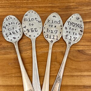 May include: Four silver spoons with engraved sayings. The spoons read "It's Parsley my fault", "Mint to bee", "Kind of a big dill", and "Thyme for me to fly".