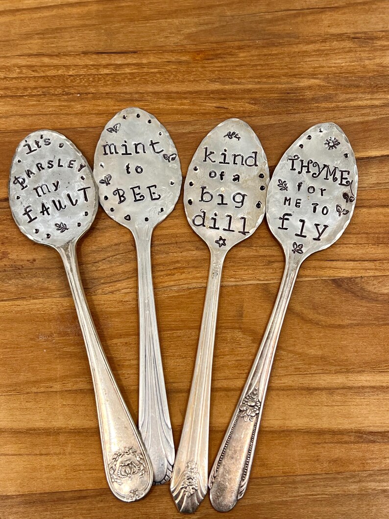 May include: Four silver spoons with engraved sayings. The spoons read "It's Parsley my fault", "Mint to bee", "Kind of a big dill", and "Thyme for me to fly".