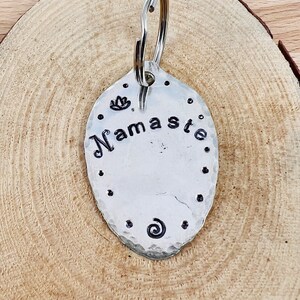 May include: Silver key chain with a hammered oval charm that says "Namaste" with a lotus flower and a swirl design.