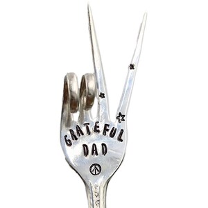 May include: A silver fork bent into the shape of a peace sign with the words "Grateful Dad" engraved on it.