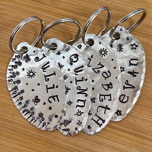 May include: Four silver oval keychains with engraved names, "Julie", "Quinn", "Isabel", and "Evan", each with a small design element like a star, sun, or tree.