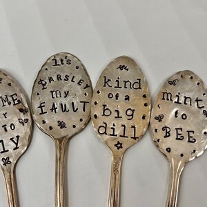 May include: Four silver spoons with engraved sayings about herbs and spices. The spoons read "It's Parsley My Fault", "Kind of a Big Dill", "Thyme for Me to Fly", and "Mint to Be".