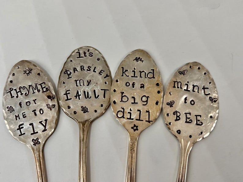 May include: Four silver spoons with engraved sayings about herbs and spices. The spoons read "It's Parsley My Fault", "Kind of a Big Dill", "Thyme for Me to Fly", and "Mint to Be".
