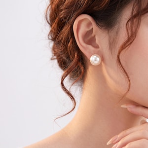 May include: A single round, lustrous white pearl stud earring with a smooth, reflective surface. The earring is secured to the earlobe, showcasing a classic spherical shape and a clean, polished finish that catches the light evenly across its surface.