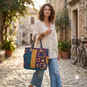 May include: A large, rectangular crochet tote bag featuring a vibrant patchwork design of teal, mustard yellow, and deep purple granny squares. The bag has two sturdy handles, gold-tone metal rings for attachment, and a scalloped top edge finish.