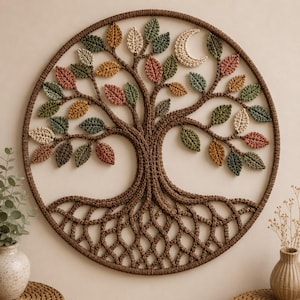 May include: A circular wall hanging featuring a crocheted tree of life design. The tree has a thick brown trunk and roots with numerous small leaves in shades of green, yellow, orange, and cream. A crescent moon is integrated into the upper branches.