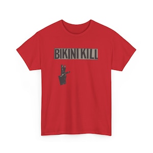 May include: Red t-shirt with the text "BIKINI KILL" in a gray rectangle above a black and gray graphic of a hand making a peace sign. The shirt is a solid red color.