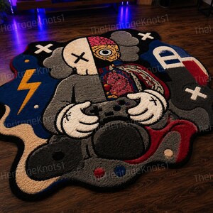 May include: A distinctive, custom-made rug with a cartoon character design. The rug features a palette of grey, black, red, blue, and beige. The character is depicted holding a game controller. The rug has an unusual shape and is placed on a wooden floor.