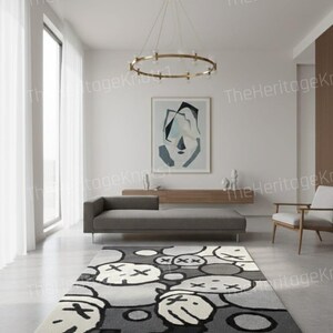 May include: A modern area rug with a repeating pattern of cartoon-like faces in shades of gray, black, and white. The rug is rectangular and placed in a contemporary living room setting. The room features a gray sofa, artwork, and a gold chandelier.