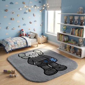 K&ouml;nnte beinhalten: Ein grauer Teppich mit einem Cartoon-Charakter-Design in einem Kinderzimmer. Die Figur hat einen wei&szlig;en Kopf, einen schwarzen K&ouml;rper und blaue Handschuhe. Das Zimmer hat ein Bett, Regale mit Spielzeug und Wolken-Dekorationen.