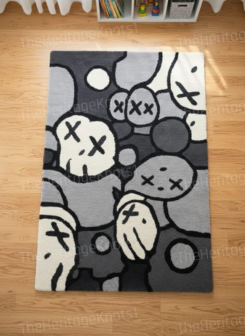 May include: A rectangular rug with a repeating pattern of cartoon-like figures in shades of gray, white, and black. The figures have X-shaped eyes and mouths. The rug is placed on a wooden floor.