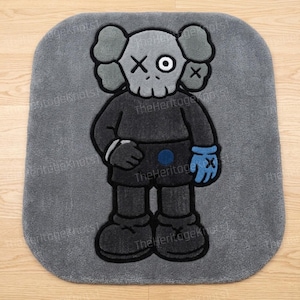 K&ouml;nnte beinhalten: Grauer rechteckiger Teppich mit einer Cartoonfigur mit sch&auml;del&auml;hnlichem Gesicht, X-f&ouml;rmigen Augen und einem blauen Handschuh. Die Figur tr&auml;gt ein dunkelgraues Outfit mit schwarzen Umrissen. Der Teppich hat abgerundete Ecken.