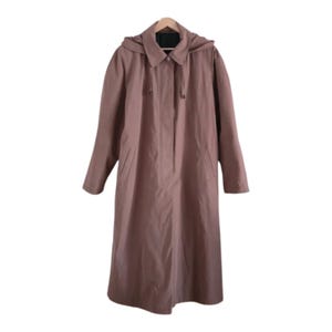 Op de afbeelding: Een lange, stoffige roze jas met een capuchon, hangend aan een houten hanger. De jas heeft een knoopsluiting en zakken. De jas is een klassieke stijl, geschikt voor diverse weersomstandigheden.