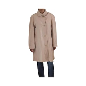 Könnte beinhalten: Beigefarbener Trenchcoat mit Knopfleiste, Kragen und langen Ärmeln. Der Mantel ist knielang und scheint aus leichtem Material zu sein. Die Person trägt eine blaue Jeans.