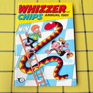 May include: The Whizzer and Chips Annual 1981 book features a cover illustration of two cartoon characters on a snakes and ladders board. One character climbs a ladder while the other slides down a large red and yellow snake. The title is in bold.