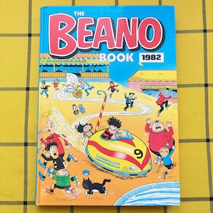 May include: The Beano Book 1982 hardback book features a colourful comic illustration on the front cover. The artwork depicts various cartoon characters in a fairground setting, with a yellow and red dodgem car numbered 9 as the central focus.