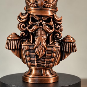 May include: A copper-colored bust of a skeletal nutcracker figure wearing a military-style uniform with epaulets, a tall hat with a central emblem, and a detailed mustache and beard, presented as a solid decorative figurine.