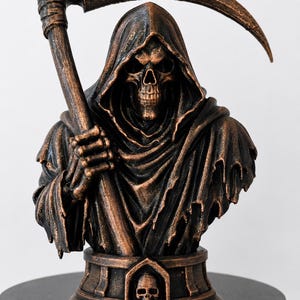 May include: A bronze-colored resin bust of a hooded grim reaper figure holding a large scythe. The figure features a skeletal face and tattered robes. The base of the statue includes a small, centered skull emblem within an arched architectural frame.