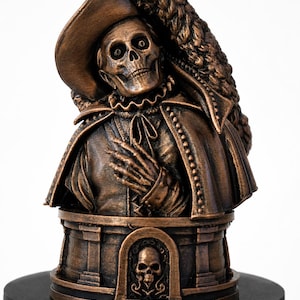 May include: A bronze-colored bust of a skeleton wearing a wide-brimmed hat with a large plume and a high-collared cape. The figure has one hand placed on its chest. The base features a small arched alcove containing a sculpted skull relief.