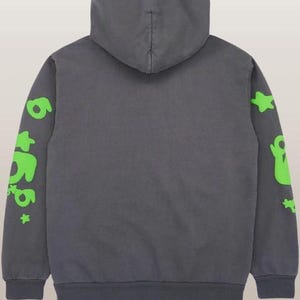 May include: A charcoal gray hoodie with a hood and long sleeves. The sleeves feature neon green graphics, including the number "6" and star shapes. The hoodie is made of a soft material and has a ribbed hem and cuffs.