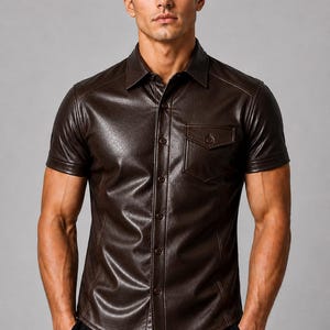 K&ouml;nnte beinhalten: Ein dunkelbraunes, kurz&auml;rmeliges Hemd mit Knopfleiste aus einem glatten, lederartigen Material. Das Hemd verf&uuml;gt &uuml;ber einen klassischen Kragen, eine Brusttasche mit gekn&ouml;pfter Klappe und sichtbare vertikale N&auml;hte auf der Vorderseite.