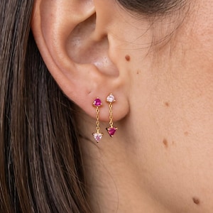 May include: Two gold chain earrings featuring small triangular gemstones. One earring has a deep pink stone at the top and a light pink stone at the bottom. The other earring has a light pink stone at the top and a deep pink stone at the bottom.