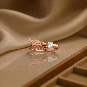 Silver angel wing diamond ring displayed in a luxury brown satin Jewelry box, featuring a detailed wing design beside a round centre stone on a slim polished silver band. A beautiful ring for promise, anniversary, bridal Jewelry, daily wear, angel inspired Jewelry, and fine Jewelry gifting. Perfect for buyers looking for a silver wing ring with clean sparkle and handmade style.