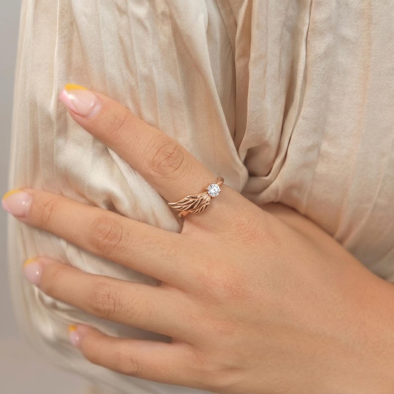 Silver angel wing diamond ring displayed in a luxury brown satin Jewelry box, featuring a detailed wing design beside a round centre stone on a slim polished silver band. A beautiful ring for promise, anniversary, bridal Jewelry, daily wear, angel inspired Jewelry, and fine Jewelry gifting. Perfect for buyers looking for a silver wing ring with clean sparkle and handmade style.
