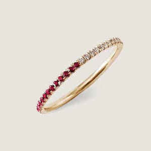 May include: A gold band ring with a row of small, red gemstones on one half and clear gemstones on the other. The ring is set against a neutral background, highlighting the jewelry's design and color.