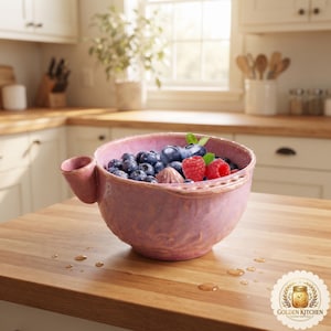 Może przedstawiać: Różowa ceramiczna miska o teksturowanej powierzchni, z małym bocznym dzióbkiem i uchwytem, wypełniona świeżymi jagodami i malinami. Miska ma zaokrąglony kształt i błyszczące wykończenie, prezentując mieszankę świeżych owoców jagodowych.