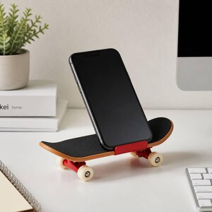 May include: A black smartphone resting on a miniature skateboard phone stand. The skateboard features a black grip tape deck, a red metal support bracket, and four small white wheels. The device is positioned upright for viewing on a desk surface.