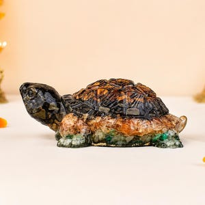 May include: A decorative turtle figurine crafted from resin and embedded with various small, multi-coloured gemstone chips. The shell features dark brown and black tones, while the body and legs incorporate shades of green, amber, and black.
