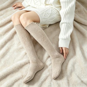 Puede incluir: Calcetines altos hasta la rodilla de color beige con puños acanalados y un patrón texturizado. Los calcetines están hechos de un material suave y se usan con un suéter y una falda blancos. Los calcetines están diseñados para la comodidad y el calor.