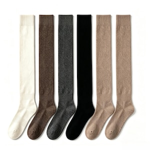 Könnte beinhalten: Sechs Paar kniehohe Socken in verschiedenen Unifarben: cremeweiß, braun, grau, schwarz und zwei Beigetöne. Die Socken sind aus geripptem Strickmaterial und vor weißem Hintergrund dargestellt.
