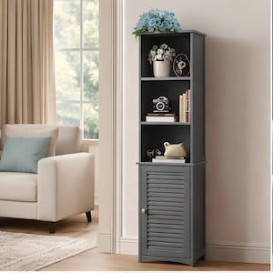 May include: A tall, dark grey storage cabinet featuring three open shelves at the top and a single lower cabinet door with horizontal slats. The shelves contain various decorative items, including a potted plant, books, and a small camera.